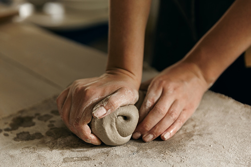 Cropped picture of an unrecognizable craftswoman using decorative rolling pin for clay work and clay decorating. Close up of craftswoman's hands imprinting pattern and decorating clay on pottery class