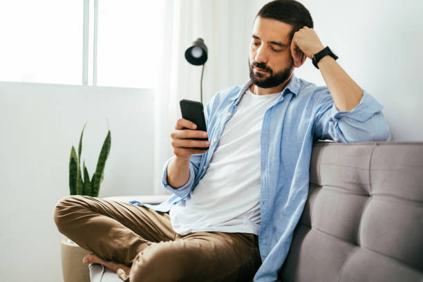 istock Young brazilian man sitting on sofa using smartphone 1418058855