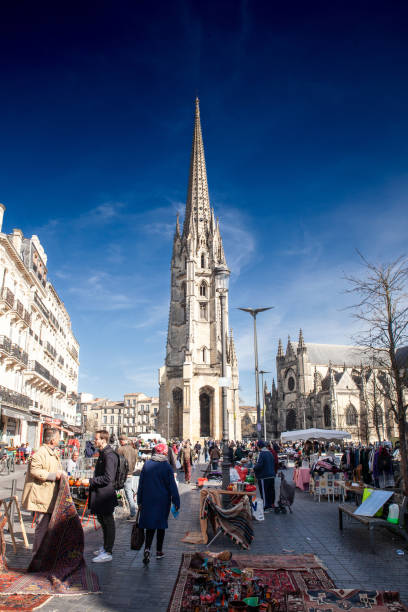 people selling second hand on marche aux puces flea market de saint michel in Bordeaux, France, with the the tower of the Basilique Saint Michel basilica in background. Picture of a sunny panorama of Bordeaux, France, with the basilique saint michel steeple and the flea market of saint michel . The Basilica of St Michael (Basilique Saint-Michel, in French), is a Flamboyant Gothic church in Bordeaux, France. fleche stock pictures, royalty-free photos & images