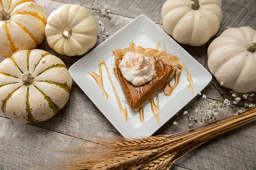 This is a close up photo of white pumpkins with Baby's Breath flowers on a wood table background with Cheesecake Pumpkin Pie and cinnamon whip cream. There is space for copy. This is a nice high key image that would work well for autumn, Thanksgiving and a holiday Halloween season in the fall.