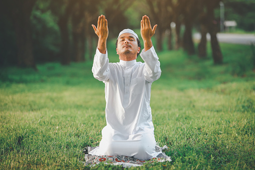 Religious muslim man  traditional kandura praying  outdoor at quiet nature  environment sun beams.