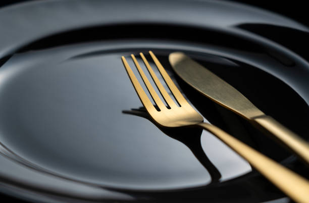 istock A golden knife and fork on a black plate. 1418072363