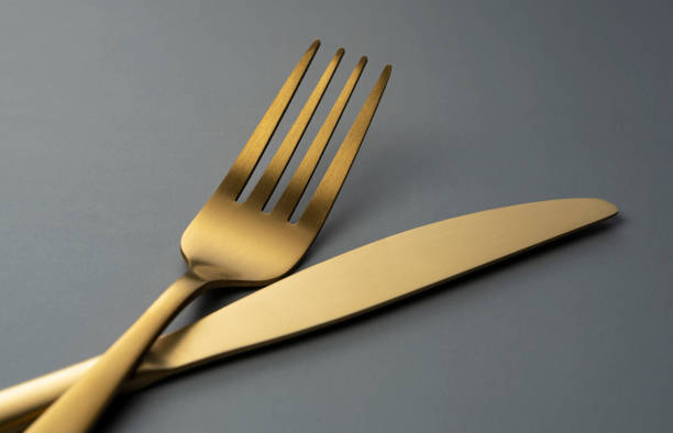 istock Gold knives and forks set against a black background. 1418072391