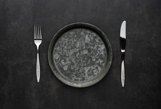 istock Silver knives and forks on a black background, empty iron plates. 1418072416