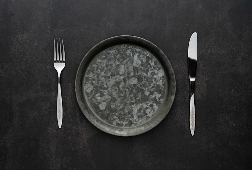 Silver knives and forks on a black background, empty iron plates. Antique, retro. View from above.