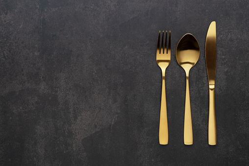 Gold knives, forks and spoons placed on a black background. Beautiful gold cutlery. View from above.
