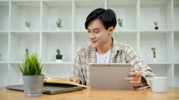istock Asian male college student in library co-working space, using digital tablet 1418085933