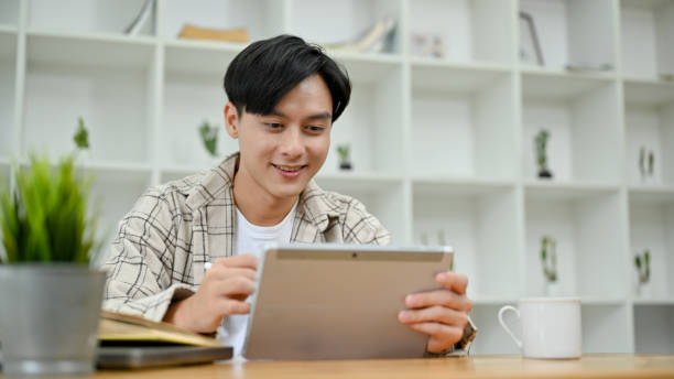 istock Handsome Asian man in causal outfit using digital tablet touchpad at his desk in office room. 1418085936