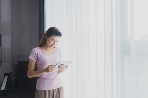 istock Asian businessman works from home using a tablet device, browsing the Internet, playing social media, Attractive businesswoman using digital tablet while standing in front of a window in home 1418088374