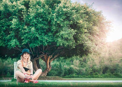 Woman is sitting beside a large tree in a park for, nature and freedom concept..