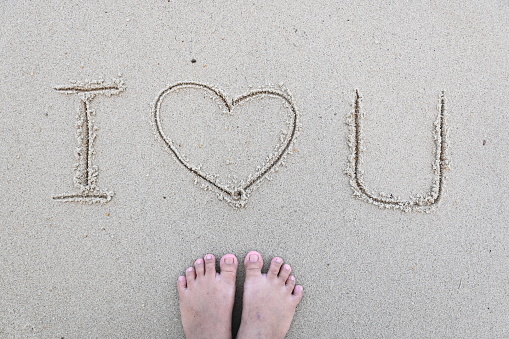 Stock photo showing writing drawn on sunny beach with word 'love' written in sand with stick in soft golden sand on seaside coastline.