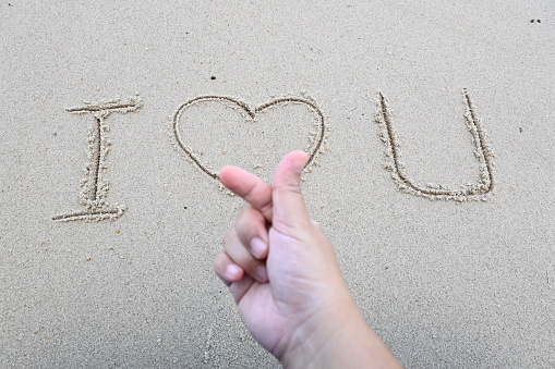 I love you writing on the beach sand and korean love symbol through finger
