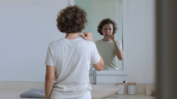 istock Routine tooth brushing. A young woman in the bathroom performs a hygiegic procedure on the surface of the enamel of the teeth from plaque with a toothbrush in front of the mirror. 1418111465
