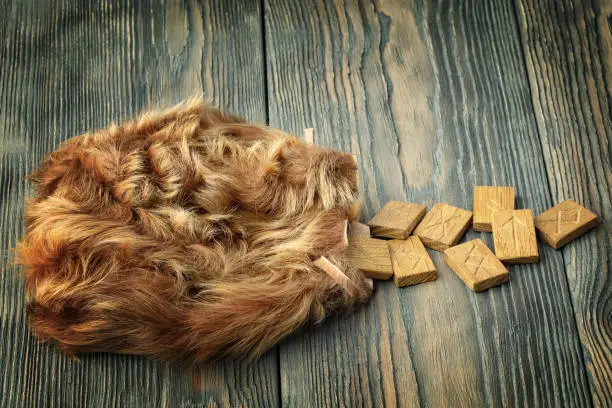 Scandinavian runes lie in a fur bag on a wooden table. Focus concept.