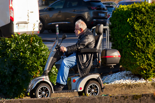 Santiago de Compostela, Spain_ December 15, 2021: Senior man driving a four-wheeled motor scooter. City street, Galicia, Spain.