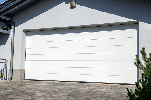 Shadows fall on a white garage door and driveway in a residential district in Surrey, British Columbia. Summer morning.