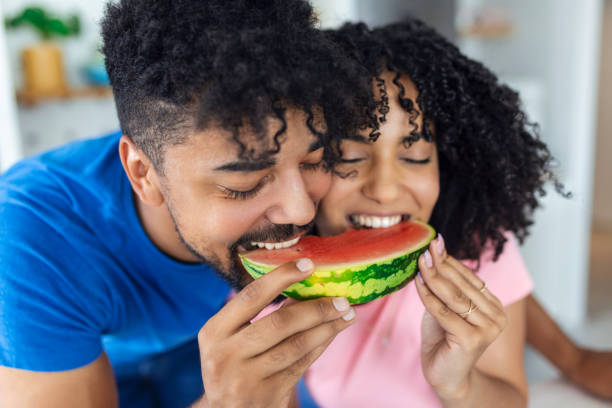 A couple in love eats a sweet watermelon in the kitchen. A man and a woman eat a ripe watermelon in the kitchen. Happy couple eating watermelon. Portrait of a couple with a watermelon Close up shot of joyful father and his little daughter looking happy while eating watermelon together. black man eating watermelon stock pictures, royalty-free photos & images
