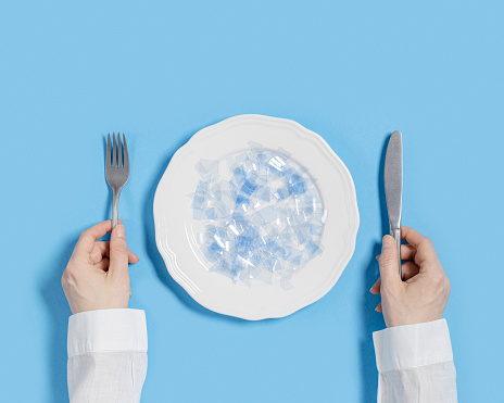 Plate with microplastics as food on blue background. Plastic pollution concept, global ocean pollution ecology problem, microplastic particles in water and food, top view, flat lay, minimal style