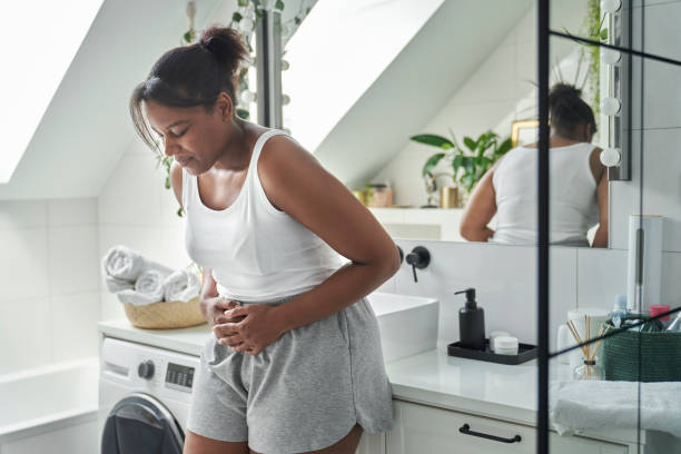 Young African-American woman standing in the bathroom and feeling pain in the stomach stock photo