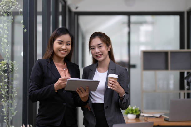 istock Two beautiful Asian businesswomen standing using digital tablet consulting and analyzing information in office work. 1418122718