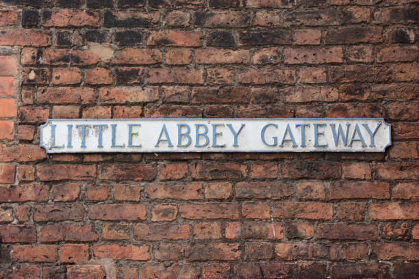 verblasstes straßennamensschild für little abbey gateway an einer roten backsteinmauer montiert - chester virginia stock-fotos und bilder