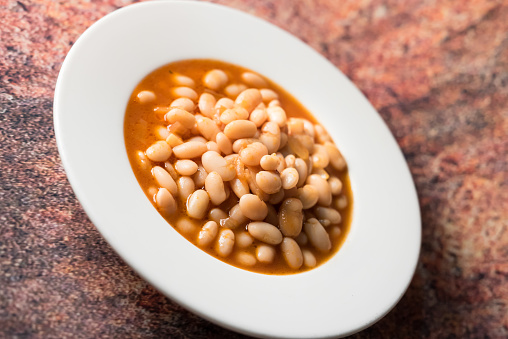 Close view of a bowl of country style baked beans in a small bowl atop a wood table top.