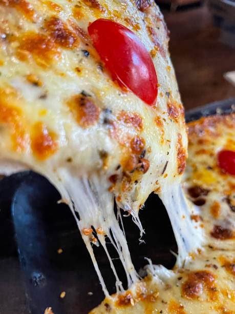 Full frame image of sliced, freshly baked Margherita pizza, stringy, melted buffalo mozzarella cheese, rich tomato marinara sauce and cherry tomato halves topping, elevated view, focus on foreground