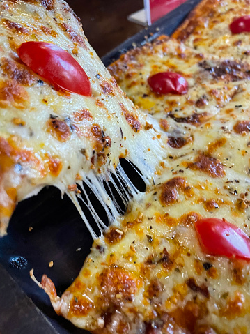 Stock photo showing close-up, elevated view of a square Margherita pizza slice topped with a rich tomato sauce, cherry tomato halves and stringy melted buffalo mozzarella.