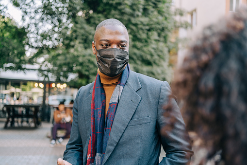 Shot of young multi-ethnic couple walking on the street in the city while wearing protective face masks for illness prevention during Covid-19 pandemic.