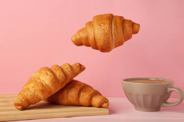 istock Flying croissant with coffee on pink background. 1418128051