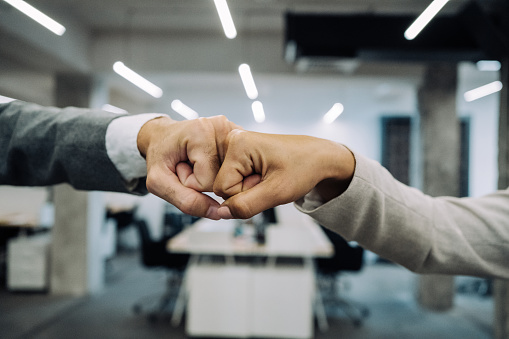 Cropped shot of a businesswoman and businessman doing fist bump greeting in the office. Unrecognizable business coworkers in the office practicing alternative greeting for safety and protection during COVID-19.