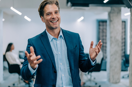 Shot of a handsome smiling businessman standing in front of his team in the office. Portrait of successful businessman standing with his colleagues working in background.
