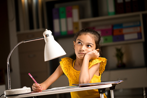 Thoughtful girl doing homework with books on desk at home