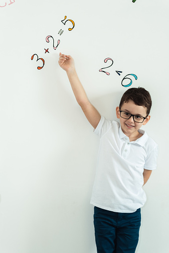 Portrait of cute caucasian schoolboy wearing glasses on the white background wall decorated with Ukrainian alphabet