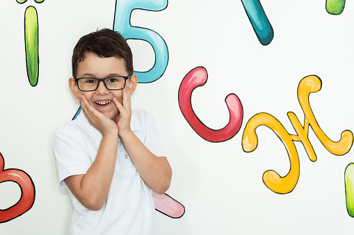 Portrait of cute caucasian schoolboy wearing glasses on the white background wall decorated with Ukrainian alphabet