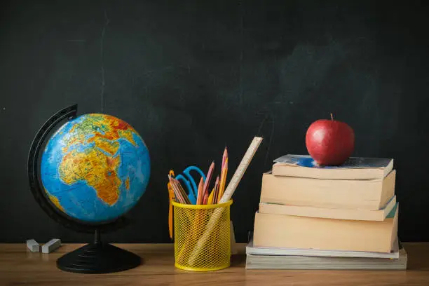 Photo of School supplies next to the globe and stack of books on the blackboard background. Back to school concept on September day
