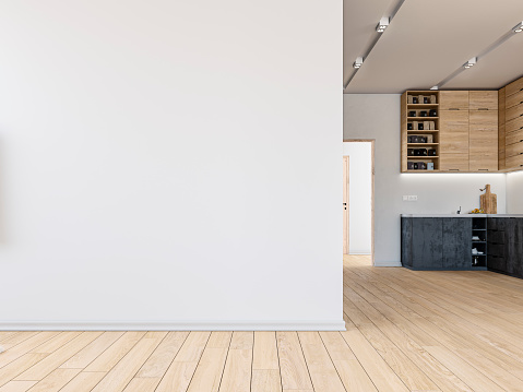 Empty living room with a large white plaster wall background with copy space on the hardwood floor. A modern kitchen in the background with high wooden cabinets and anthracite lower kitchen cabinets on a white plaster wall.  A bright hallway with doors on the side of the kitchen led light reflectors on the ceiling. 3D rendered image.