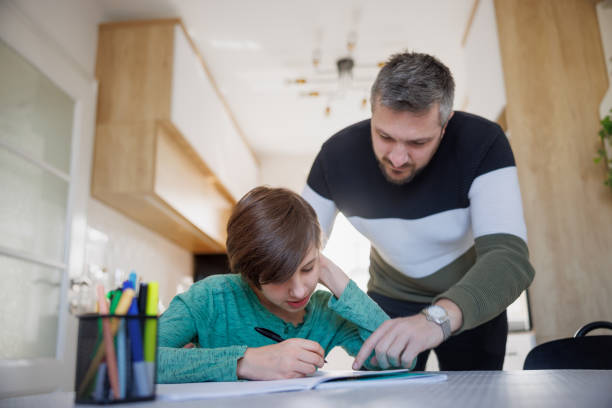 istock Father standing by his home-schooled son and pointing at his notebook on the table 1418133768