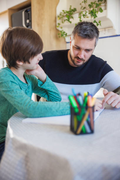 istock Tuition teacher working with home-schooled boy and pointing at work in notebook 1418133835