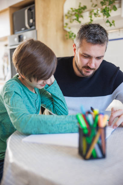 istock Tuition teacher working with home-schooled boy and checking his work in notebook 1418133839