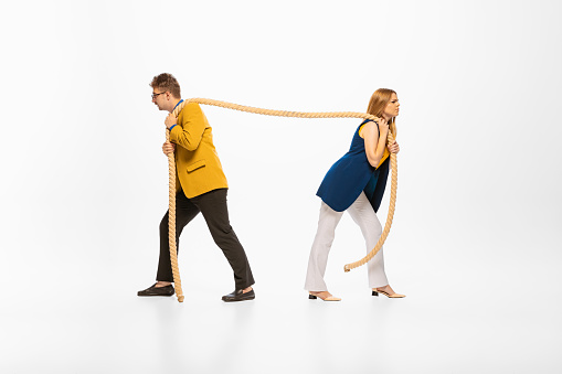 Portrait of young man and woman in official clothes pulling rope isolated over white studio background. Professional competition. Concept of human emotions, office, success, career, promotion