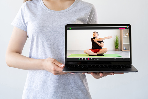 Yoga video tutorial. Online training. Indoor sport. Woman showing laptop screen with man performing stretching exercise isolated on neutral.
