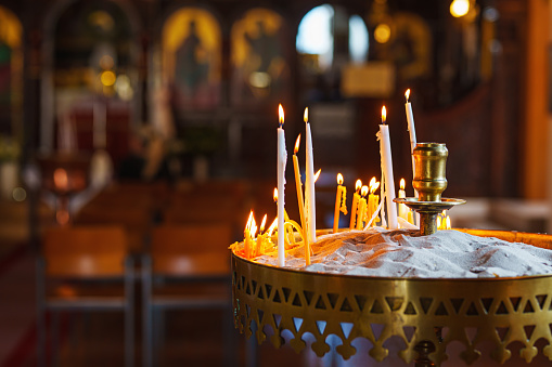 A row of lighted wax candles in the Christian Orthodox Church on a dark blurred background.