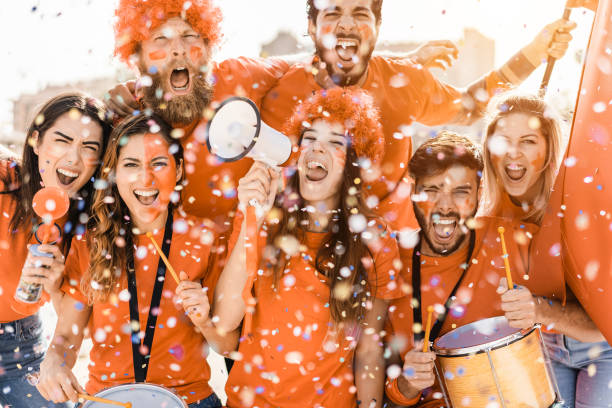 istock Orange sport fans screaming while supporting their team outside the stadium - Focus on right girls faces 1418143062