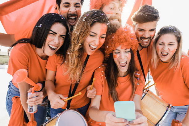 Orange sport supporters watching football game on mobile phone - Main focus on left girl face stock photo