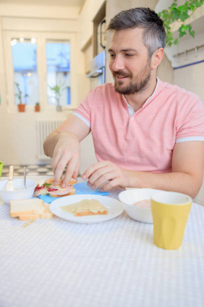 istock Happy man sitting at the table at home and making a sandwich 1418144868