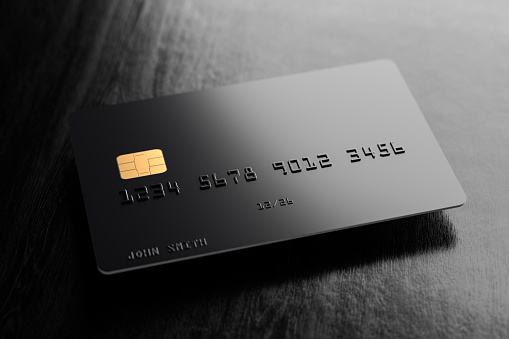 A blank black credit card with fake name (John Smith) and number (1234...) hovering over a black wood surface with shadow