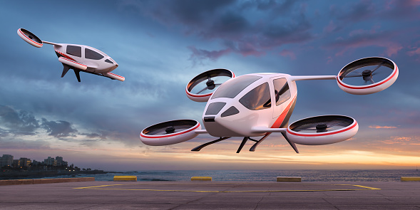 Two generic eVTOL craft in mid flight hovering at different heights, near and over a landing platform in a remote coastal location at dawn / dusk. With motion blur to rotor blades.