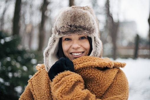 Happy young woman in yellow coat and hat enjoying falling snow and winter weather