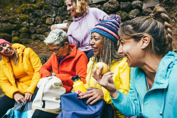 multirassische frauen, die nach dem trekkingtag im bergwald spaß haben - fokus auf afrikanisches weibliches gesicht - people eating walking fun stock-fotos und bilder